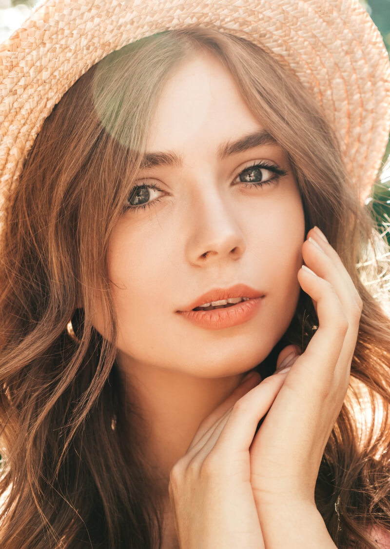 Junge Frau mit schönem Gesicht und Hut, zeigt strahlende Haut und frischen Look, ideal für Beauty-Produkte.