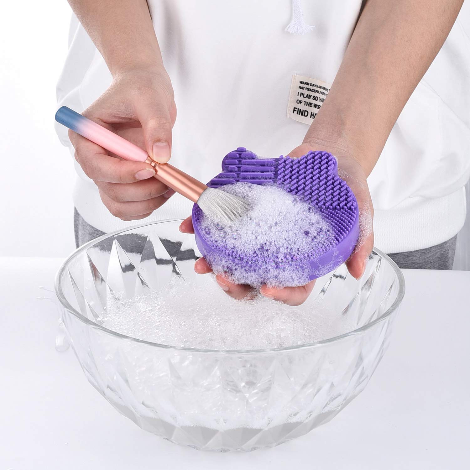 Person using Silikon-Pinselreiniger to clean makeup brush in soapy water.