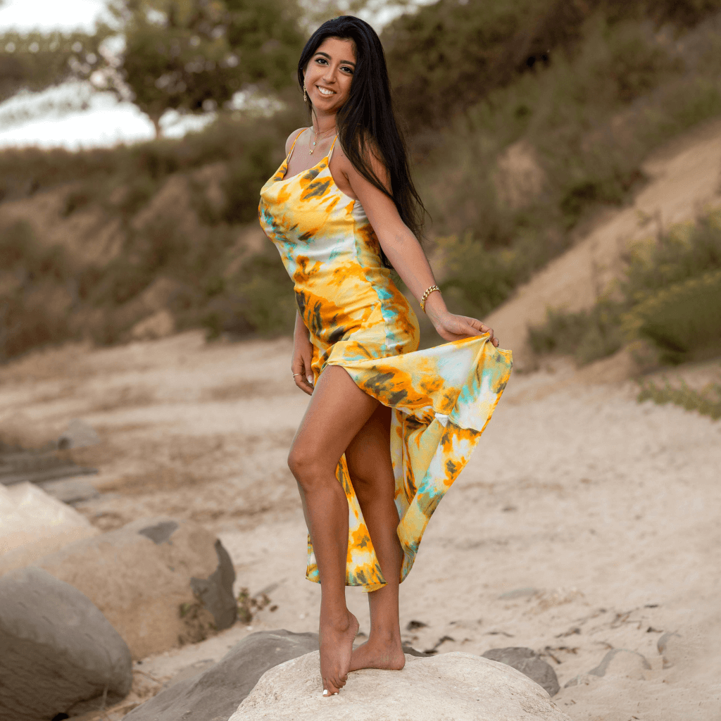 Junge Frau in einem bunten Kreppkleid, die am Strand posiert und ihren Rock anhebt.