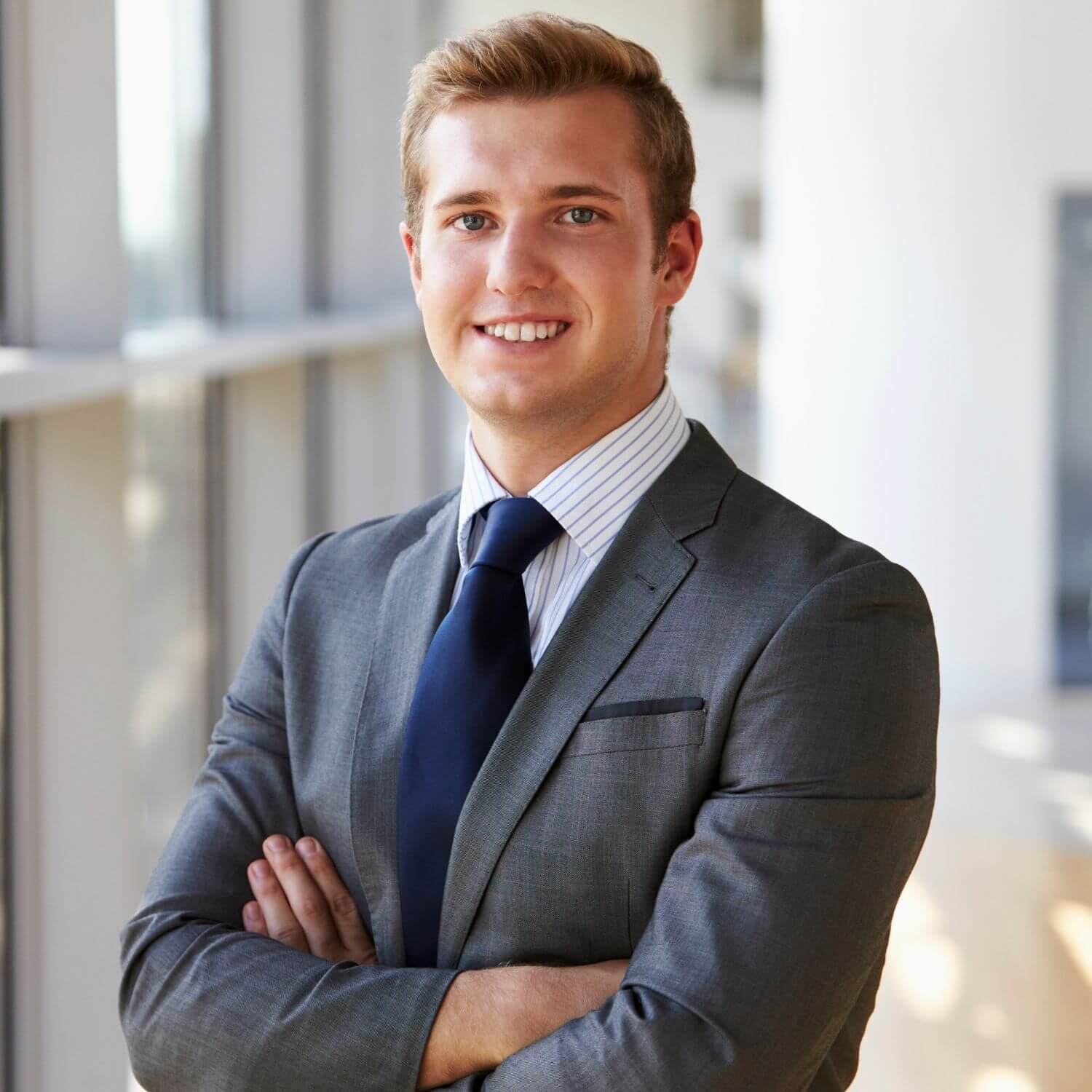 Männlicher Geschäftsmann in Anzug mit verschränkten Armen, professionelles Portrait im modernen Büro.